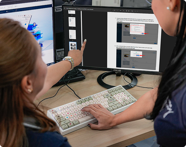 Collaborative team environment showing office staff reviewing step-by-step technical procedures on a dual-monitor setup.